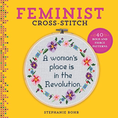 Yellow book cover showing title "Feminist Cross-Stitch," featuring a cross-stitch design of a floral wreath surrounding the phrase "A woman's place is in the Revolution"