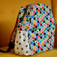 A colourful backpack with side pocket against a yellow wall.