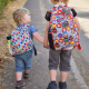 Two children wearing backpacks and walking along a sidewalk.
