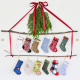 Twelve miniature Christmas stockings hanging from two branches against a white background and framed by red ribbon and cedar.