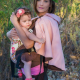 A woman wearing an elbow length pink cape and a baby in a carrier.
