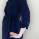 Side view of a woman in a navy blue wrap dress with three-quarter sleeves standing in front of a white wall.