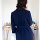 Back view of a woman in a navy blue wrap dress with three-quarter sleeves standing in front of a desk against a white wall.