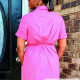 Back view of a woman in a bright pink, short sleeved wrap dress standing on a front porch.