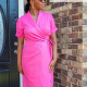 A woman in a bright pink, short sleeved wrap dress standing on a front porch.