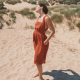 Side view of a woman in a red dress with her hands in her pockets standing on a sandy hill.