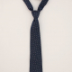A navy blue necktie laid out on a neutral-coloured flat surface.
