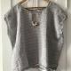 A grey, boxy top with white stripes and a white bead necklace on a clothes hanger in front of a white door.