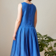 Three-quarter back-view photo of woman wearing Harper, a sleeveless dress with box-pleated skirt, in blue.