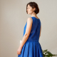 Side-view photo of woman wearing Harper, a sleeveless dress with box-pleated skirt, in blue.